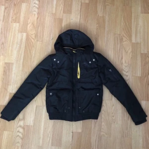 Everlast Bomber Jacket Unisex  - Snygg svart jacka från Everlast med huva och dragkedja. Jackan har flera praktiska fickor och detaljer i gult. Perfekt för kyligare dagar.