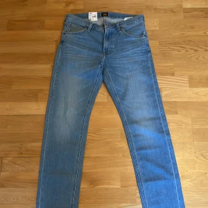Helt nya Blå jeans från Lee med prislappen kvar - Säljer ett par helt oanvända klassiska blå jeans från Lee, modell Daren Zip Fly. De har en rak passform och är tillverkade i ett hållbart material med Indigood-teknologi. Perfekta för en avslappnad stil.