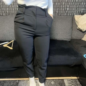 Svarta kostymbyxor - Snygga svarta kostymbyxor med hög midja och en elegant passform. Perfekta för en stilren look. Byxorna har en klassisk design med raka ben och är tillverkade i ett bekvämt material.