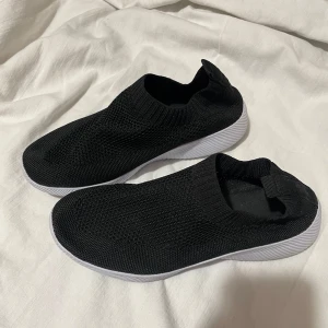 Svarta idrott sneakers - Säljer ett par svarta stickade sneakers med vit sula. Skorna har en enkel och stilren design utan snörning, vilket gör dem lätta att ta på och av. Perfekta för en avslappnad stil. Jätte sköna skor att ha på gymmet 
