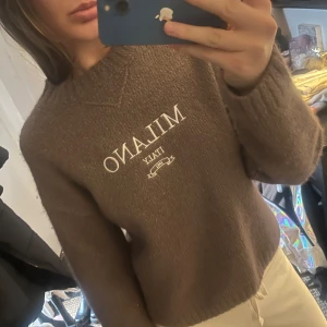 Stickad tröja med motiv - Säljer en brun tröja med texten 'Milano Italy' på framsidan. Tröjan har en rund hals och långa ärmar, perfekt för en avslappnad stil. Den är mjuk och bekväm, idealisk för kyligare dagar. Jag har bara använt den en gång så den är så gott som orörd. Den är utav bomull så för känsliga kan den stickas lite. Den är köpt för 500kr men pris kan diskuteras 