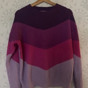 Flerfärgad stickad tröja - Säljer en mysig stickad tröja i flera färger, inklusive lila, rosa och vinröd. Tröjan har ett randigt mönster och långa ärmar, perfekt för kyligare dagar. Den är både stilren och bekväm.använd i sparsamt användning.