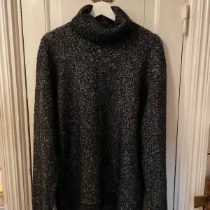 Grå stickad tröja från Ermenegildo Zegna - Säljer en elegant grå stickad tröja från Ermenegildo Zegna, tillverkad i Italien. Tröjan är gjord av en lyxig blandning av ull, kashmir och silke, vilket ger en mjuk och varm känsla. Perfekt för kyliga dagar med sin polokrage och långa ärmar.