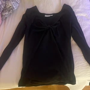 Svart långärmad topp från Vila - Säljer en stilren svart långärmad topp från Vila. Toppen har en elegant knutdetalj framtill som ger en fin touch. Perfekt för både vardag och speciella tillfällen. 🖤