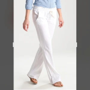 Roxy Vita linnebyxor - Roxy Snygga och bekväma vita linnebyxor med knytband i midjan. Perfekta för en avslappnad stil med en loose passform och hög midja. Passar utmärkt till sommarens varma dagar.