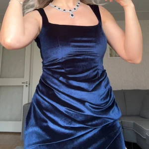 Mörkblå sammet klänning med slits - Elegant mörkblå långklänning i sammet med en stilren design. Klänningen har en smickrande passform och en djärv slits framtill. Den är ärmlös och perfekt för festliga tillfällen. Passar 36-34