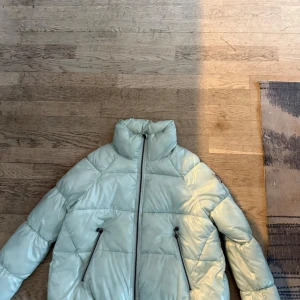 Ljusgrön pufferjacka - Snygg ljusgrön pufferjacka med dragkedja och hög krage. Perfekt för kyliga dagar med sin quiltade design och praktiska fickor med dragkedjor.