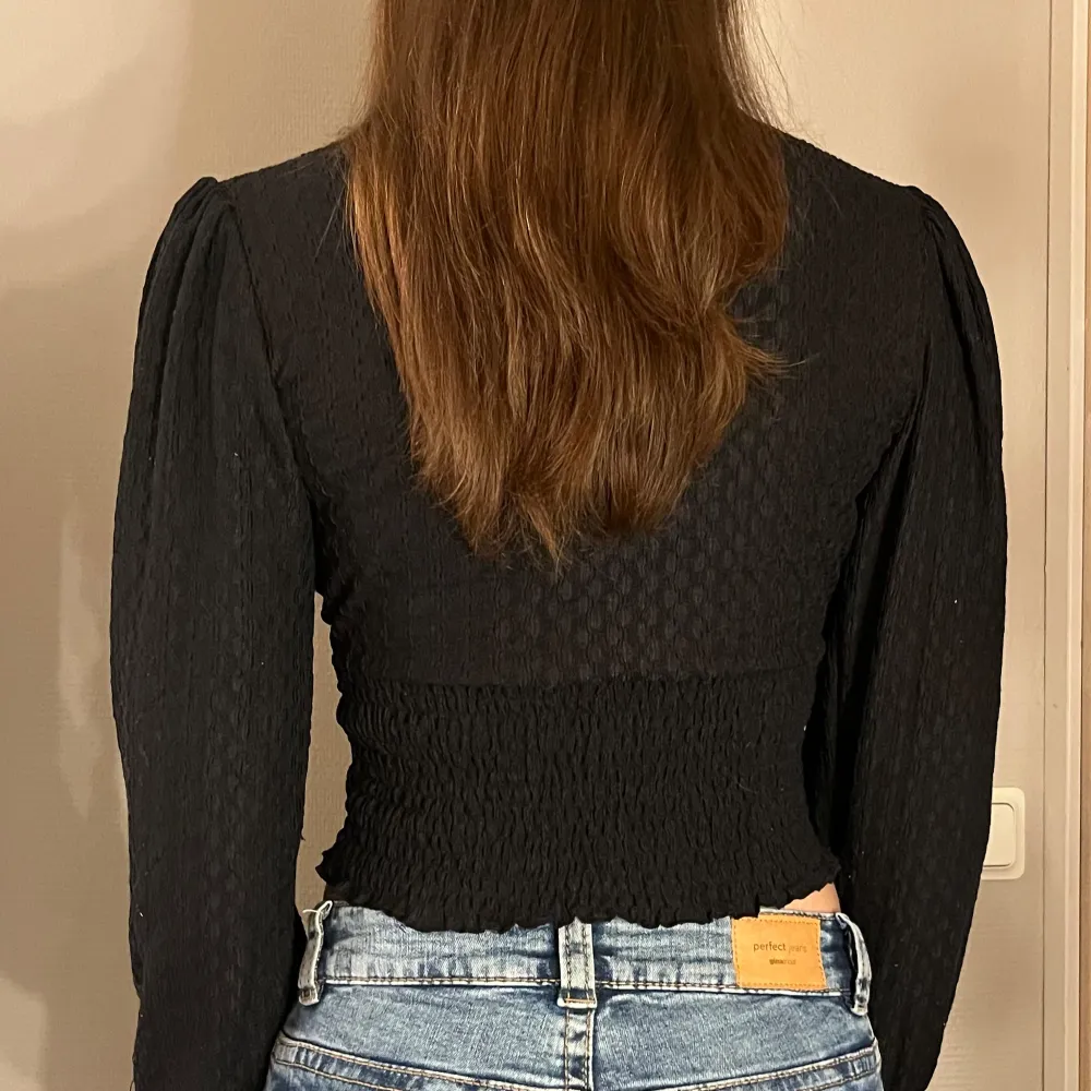Snygg svart v-ringad topp från ONLY med långa ärmar och en croppad passform. Toppen har en ribbad struktur och elastisk midja som ger en smickrande silhuett. ✨. Yläosat.