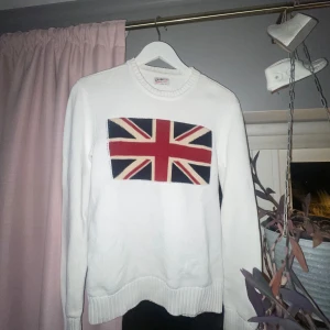 Vit stickad tröja med Union Jack-motiv - Säljer en vit stickad tröja med ett stort Union Jack-motiv på bröstet. Tröjan har långa ärmar och ribbstickade muddar vid ärmslut och nederkant. Perfekt för en stilren och klassisk look.