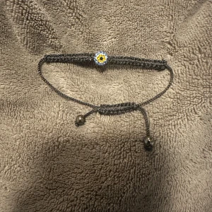 Svart armband med onda ögat - Charmigt svart armband med en liten onda ögat i mitten. Armbandet har justerbara band med små pärlor i ändarna för en perfekt passform.
