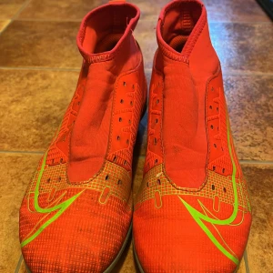 Röda Nike Mercurial fotbollsskor. storlek 38 - Snygga röda Nike Mercurial fotbollsskor med gröna detaljer. Skorna har en strömlinjeformad design och är perfekta för snabba rörelser på planen. De har en elastisk passform utan snörning för enkel på- och avtagning. Storlek 38. Använda i bra skick