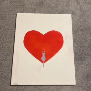 Tavla med rött hjärta - En stilren tavla med ett stort rött hjärta i mitten. Motivet inkluderar en liten figur i grått som klättrar på hjärtat. Bakgrunden är vit, vilket framhäver hjärtat och figuren. Perfekt för att ge en färgklick till rummet.