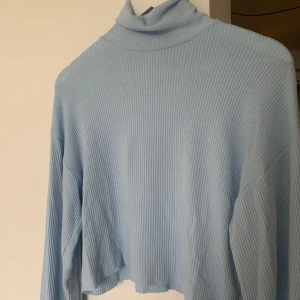 Ljusblå tröja med polokrage - Ljusblå långärmad tröja från Bershka. Högkrage, polo. Ribbat material. Använd 1 gång.