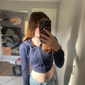 Mörkblå croppad hoodie från Divided - Säljer en snygg mörkblå croppad hoodie från Divided. Den har en dragkedja framtill och långa ärmar. Perfekt för en avslappnad stil och passar bra till jeans eller leggings. Superbekväm och trendig!