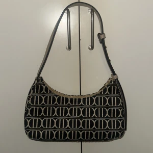 Svart och beige axelväska med mönster - Säljer en snygg axelväska i svart och beige med ett coolt mönster. Väskan har en justerbar axelrem och en dragkedja upptill. Perfekt för både vardag och fest! Fått även massvis med koplimanger av denna väskan. Köpt för 350 kr i tyskland och säljs 250