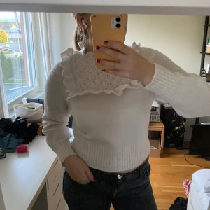 Vit stickad tröja från & Other Stories - Säljer en superfin vit stickad tröja från & Other Stories. Den har en unik design med volangdetaljer runt halsen och ett vackert stickat mönster på bröstet. Tröjan är långärmad och perfekt för både höst och vinter. Den är i nyskick och väldigt mysig att ha på sig!