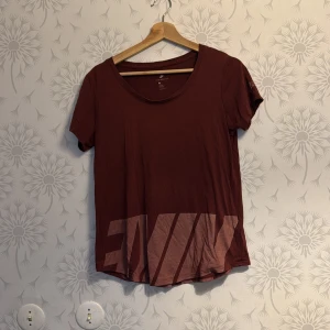 Vinröd  t-shirt från Nike - Säljer en brun t-shirt från Nike med korta ärmar och ett stort tryck i ljusare nyans på framsidan. Perfekt för en avslappnad stil. Passar bra till jeans eller träningsbyxor.