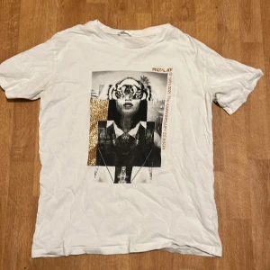 Vit t-shirt med tryck från Replay - Säljer en vit t-shirt från Replay med ett unikt tryck på framsidan. Trycket har en mix av svartvita och färgade element, inklusive ett tigeransikte och text. Perfekt för en cool och avslappnad stil.