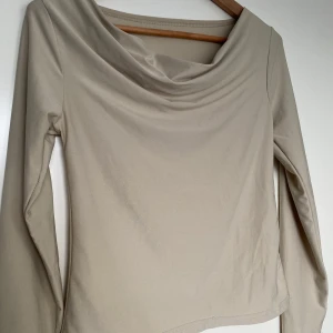 Beige långärmad topp - Snygg beige långärmad topp med draperad halsringning, vattenfallseffekt. Perfekt för en stilren look. Bekvämt och stretchigt material. 