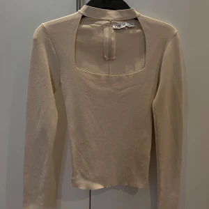 Beige långärmad topp från Zara - Elegant beige topp från Zara med långärmad design och en unik öppen detalj framtill. Toppen har en lite högre hals. Använd 1 gång 💕