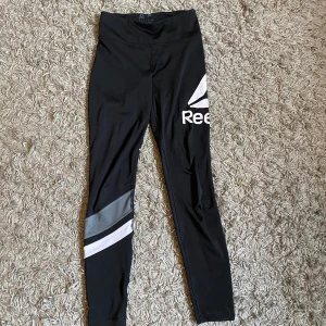 Svarta leggings från Reebok - Snygga svarta leggings från Reebok med stora logotyper på benen. Säljer då jag inte använder dem längre. Med tanke på att trycket har lossat lite på baksidan säljer jag dem för endast 30kr