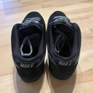 Nike SB Dunk Low Pro i svart och grå - Säljer ett par Nike SB Dunk Low Pro i svart och grå. Skorna har en klassisk design med snörning och en slitstark gummisula i gult. Perfekta för både skate och vardag.