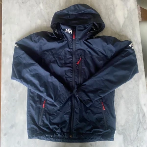 Helly Hansen seglarjacka vindjacka regn jacka mörkblå  - Skick: 7,5/10. Delar av helly Hansen märket i nacken samt ryggen har släppt lite, det är dock inget som märks. Från märket helly Hansen i storlek M. Om du är osäker på om det kommer att passa kan du alltid fråga om mått! 