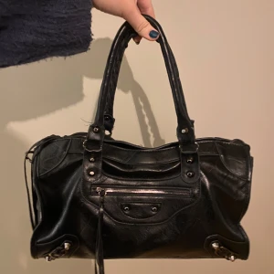 Svart handväska med dragkedja - Tveka inte med att skicka prisförslag! 🔥 Snygg svart handväska i skinn med dragkedja och nitar. Väskan har dubbla handtag och en stilren design som passar perfekt för en chic look. Fen är litr sliten i handtagen, men inget jag tänker på.