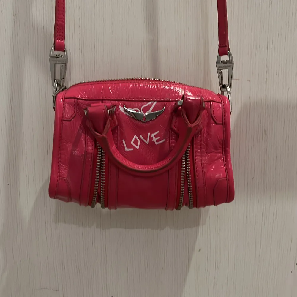Snygg rosa axelväska med texten 'LOVE' och 'ZADDICTED' tryckt på framsidan och sidan. Väskan har dubbla handtag och en justerbar axelrem. Den är utrustad med dragkedjor och har en cool, glansig finish.. Laukut & Käsilaukut.