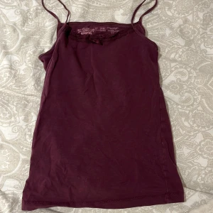 Vinröd linnetopp från Papaya - Säljer en söt vinröd linnetopp från Papaya med spetsdetaljer och en liten rosett framtill. Toppen har smala axelband och är tillverkad i bomullsmaterial för en bekväm känsla. Perfekt för varma dagar eller som ett lager under andra plagg.