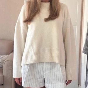 Vit stickad tröja - Säljer en mysig vit stickad tröja med långa ärmar och ribbade detaljer vid ärmslut och nederkant. Perfekt för kyligare dagar och ger en stilren look. Passar bra till både jeans och kjol.