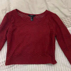 Röd långärmad topp från Forever 21 - Snygg röd topp från Forever 21 med långärmad design och ett unikt hålmönster. Perfekt för att lägga till en touch av stil till din garderob. Toppen har en rund halsringning och är tillverkad i ett bekvämt material.