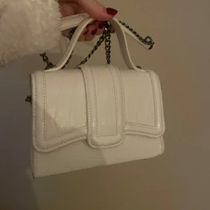 Vit väska från zara - Snygg vit axelväska med krokodilmönster och kedjedetaljer. Väskan har ett elegant handtag och en stilren design som passar perfekt för en chic look. Perfekt för att lyfta din outfit med en touch av elegans.Väskan är från zara och använd 1 gång 