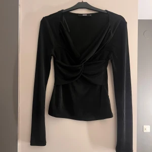 Svart långärmad topp från BikBok - Snygg svart långärmad topp från BikBok med omlott-design och knytdetalj framtill. Perfekt för en stilren look. Tillverkad i ett mjukt och bekvämt material.