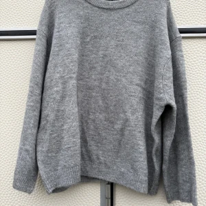 Grå stickad tröja - Säljer en stilren grå stickad tröja med rund hals och långa ärmar. Perfekt för kyligare dagar och enkel att matcha med olika outfits. Tröjan har ribbade muddar vid ärmslut och nederkant för en bekväm passform.