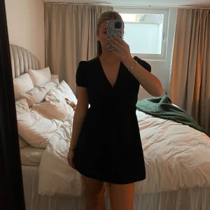 Svart kortklänning med öppen rygg - Snygg svart kortklänning med v-ringning och öppen rygg. Klänningen har korta ärmar och knytning i ryggen, vilket ger en elegant touch. Perfekt för en kväll ute eller en speciell tillställning.