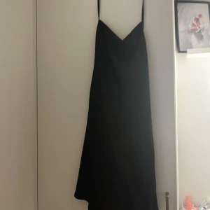 Svart axelbandslös klänning - Snygg svart axelbandslös klänning med smala axelband. Perfekt för en elegant kvällslook. Klänningen har en enkel och stilren design som gör den lätt att matcha med accessoarer.