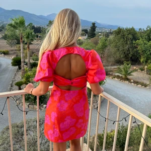 Rosa blommig klänning med öppen rygg - Snygg kort rosa klänning med stora blommor i rosa. Den har puffiga kortärmar och en trendig öppen rygg. Perfekt för alla tillfällen!