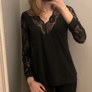 Svart blus med spetsdetaljer - Elegant svart blus med v-ringning och spetsdetaljer på ärmar och hals.  Vet inte vart den är ifrån, men aldrig använd. I storlek S. Hör av er vid frågor🥰