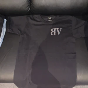 Svart bvaldi T-shirt  - Snygg svart t-shirt med glittrig text 'BV' på framsidan och 'Need Money for Porsche' på baksidan. Perfekt för en cool och avslappnad stil. Alla pärlor sitter kvar