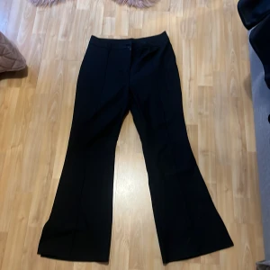 Svarta kostymbyxor från Shein  - Snygga svarta kostymbyxor från Shein i damstorlek L.  Byxorna har en klassisk design med hög midja och bootcut-stil. De är försedda med en knapp och dragkedja framtill för enkel stängning.