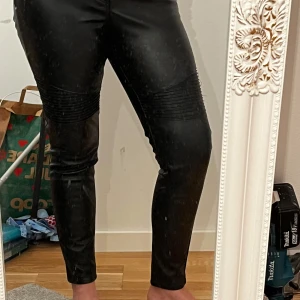 Svarta skinnbyxor med ribbade detaljer - Snygga svarta skinnbyxor med tight passform och ribbade detaljer vid knäna. Perfekta för en trendig look.