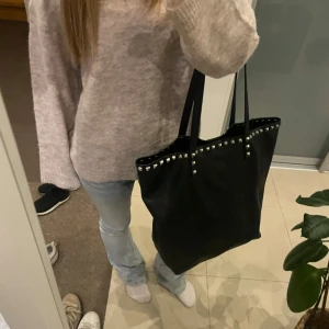 Svart väska - En snygg väska med nitar i bra skick. Lite liknande en valentino väska med silvernitar. Får plats med mycket till exempel skolmappar och dator. Säljer pga att den ej kommer till användning!