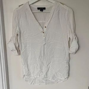 Vit blus - En vit lös blus med halva harmar och snygg guld detalj.