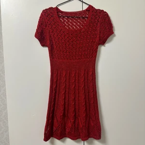 Julröd stickad klänning - Charmig röd stickad klänning med korta ärmar och ett vackert mönster som glittrar. Perfekt för kyligare dagar med sin mysiga och stiliga design. Finns i marinblå och champagne färg! Passar storlek XS-S
