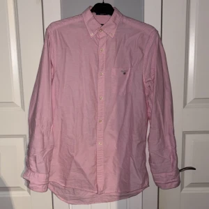 Rosa skjorta från GANT - Snygg rosa Oxford-skjorta från GANT med broderad logga på bröstfickan. Skjortan har långa ärmar och klassisk krage med knappar. Perfekt för en stilren look.