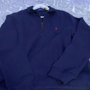 Mörkblå tröja Polo Ralph Lauren - Snygg mörkblå tröja från Polo Ralph Lauren med dragkedja vid halsen och det klassiska röda logotypbroderiet på bröstet. Perfekt för en stilren och avslappnad look.