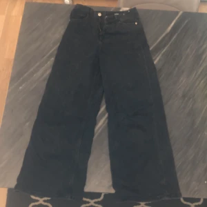 Svarta jeans med vida ben - Snygga svarta jeans med hög midja och vida ben. Perfekta för en avslappnad stil. Klassisk design med knappar och dragkedja framtill.
