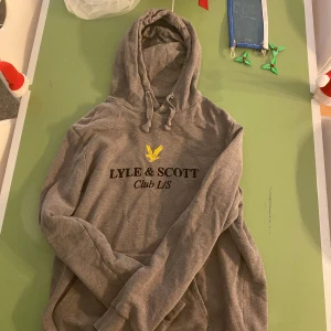 Grå hoodie från Lyle & Scott - Säljer en stilren grå hoodie från Lyle & Scott med justerbar huva och tryck framtill. Perfekt för en avslappnad look. 🐥9/10 skick. Pris diskuteras!
