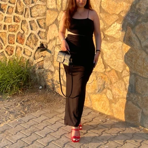 Svart långklänning med smala axelband 40 - Elegant svart långklänning med smala axelband och en figurnära passform. Perfekt för en kväll ute eller en speciell tillställning. Kombinera med färgglada accessoarer för en stilfull look.